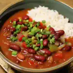 1. Hearty vegetarian chili with kidney beans, fresh chopped green onions, and served with white rice in a black bowl.