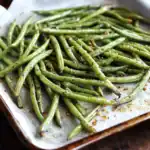 Roasted green beans seasoned with garlic, salt, and pepper on parchment paper. Perfect healthy side dish or snack with crispy texture and savory flavor. Ideal for meal prep and appetizer options.