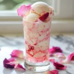 Creamy vanilla ice cream with pink swirl served in a tall glass topped with rose petals, perfect for spring desserts or romantic celebrations.