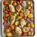 Juicy baked chicken breasts with roasted colorful vegetables including potatoes, cherry tomatoes, green beans, bell peppers, and red onion on a baking sheet. Perfect for a healthy, flavorful dinner.