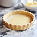 Buttery pie crust with fluted edges on a marble surface, ready for filling.