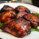 Succulent barbecued chicken thighs with crispy skin on a white plate, garnished with fresh greens, perfect for outdoor grilling and summer recipes.