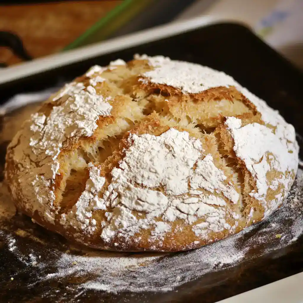 Freshly baked bread with a golden crust, dusted with powdered sugar, on a baking tray. Perfect for breakfast or a snack, this homemade bread combines a crispy exterior with a soft, airy interior.