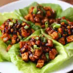 Sichuan chicken lettuce wraps, stir-fried chicken with vegetables, savory sauce, garnished with green onions, served on fresh lettuce leaves for healthy, flavorful Asian-inspired appetizer.