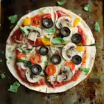 Fresh veggie pizza with mushrooms, black olives, cherry tomatoes, bell peppers, and basil on a crispy crust. Perfect for a quick homemade meal or party snack. Enjoy this flavorful vegetarian pizza recipe from Station Recipes.
