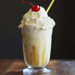 Creamy banana pineapple milkshake topped with whipped cream and cherry, served in a tall glass for a delicious summer refreshment.