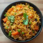 Steamed vegetable fried rice with carrots, green peas, and cilantro in a black bowl, showcasing healthy, flavorful rice recipes ideal for lunch or dinner.