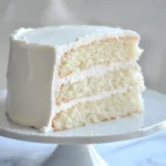 Fluffy white vanilla cake with creamy frosting layers on a white cake stand.