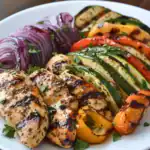 Juicy grilled chicken breast served alongside colorful roasted zucchini, red bell peppers, yellow squash, and red onions, garnished with fresh parsley for a healthy, flavorful meal.
