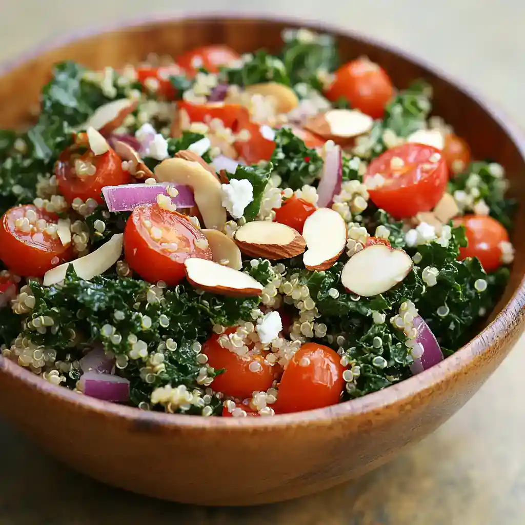 Bright, fresh vegan kale salad with cherry tomatoes, sliced almonds, red onions, quinoa, and feta cheese, dressed with lemon vinaigrette. Perfect for healthy eating and plant-based meals.