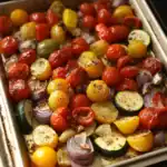 Colorful oven-roasted cherry tomatoes, zucchini, onion, and bell peppers in a baking dish, seasoned with herbs and spices, perfect for easy, healthy side dishes or meal prep.