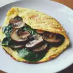 A delicious fluffy mushroom omelette filled with sautéed mushrooms and fresh spinach, seasoned to perfection for a healthy breakfast or brunch option.