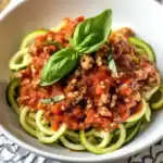 Delicious homemade spaghetti with savory Bolognese sauce topped with fresh basil leaves, served in a white bowl perfect for dinner or lunch.