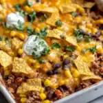 Delicious cheesy taco casserole with ground beef, black beans, corn, and melted cheddar cheese, topped with sour cream, cilantro, and crunchy tortilla chips. Perfect for a quick, flavorful family dinner or party dish.