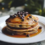 Scrumptious stack of fluffy pancakes topped with chocolate chips, drizzled with syrup, perfect for breakfast or brunch. Easy homemade pancake recipe from Station Recipes.