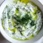 Delicious creamy cucumber and dill yogurt dip garnished with fresh dill and a drizzle of olive oil, perfect for snacks or appetizers.