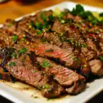 Juicy grilled beef steak topped with fresh herbs and savory sauce, served on a white plate. Perfect for a hearty and flavorful main dish, showcasing perfectly cooked, tender beef with appetizing garnishes.