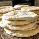 Delicious homemade naan bread stacked on a marble surface, showcasing its soft, fluffy texture and golden-brown spots perfect for Indian cuisine, sandwiches, or side dishes.