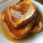 Delicious French toast topped with powdered sugar and drizzled with syrup on a white plate, perfect for breakfast or brunch.