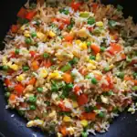 Colorful vegetable fried rice with carrots, peas, corn, and scrambled eggs, cooked in a wok. Perfect for a quick, healthy meal or side dish.
