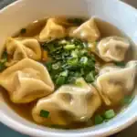 Tasty homemade dumpling soup garnished with fresh green onions, served in a white bowl, perfect for comforting meals and warm cravings.