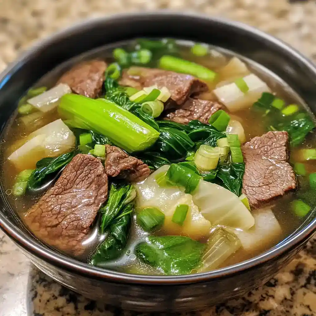 Hearty beef and vegetable soup with tender beef chunks, leafy greens, and potatoes in a clear broth. Perfect for comforting meals and easy to prepare.