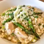 A creamy chicken and asparagus risotto topped with grated Parmesan cheese, garnished with fresh herbs. Perfect for a comforting and flavorful meal.