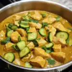 Delicious chicken curry with fresh cucumber slices and cilantro, served in a stainless steel pan, showcasing a flavorful and hearty dish perfect for dinner.