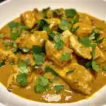 Delicious chicken curry with rich, flavorful sauce garnished with fresh cilantro, served in a white bowl. Perfect for a hearty meal.