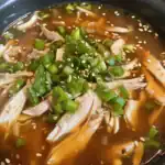 Delicious shredded chicken soup garnished with chopped green onions and sesame seeds, served in a flavorful broth. Perfect for a comforting meal.