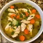 A bowl of homemade chicken vegetable soup with carrots, celery, and herbs in a clear broth, perfect for a comforting and nutritious meal.