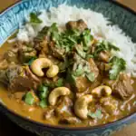 Delicious beef curry served with fluffy white rice, garnished with fresh cilantro and cashew nuts, perfect for a hearty meal.