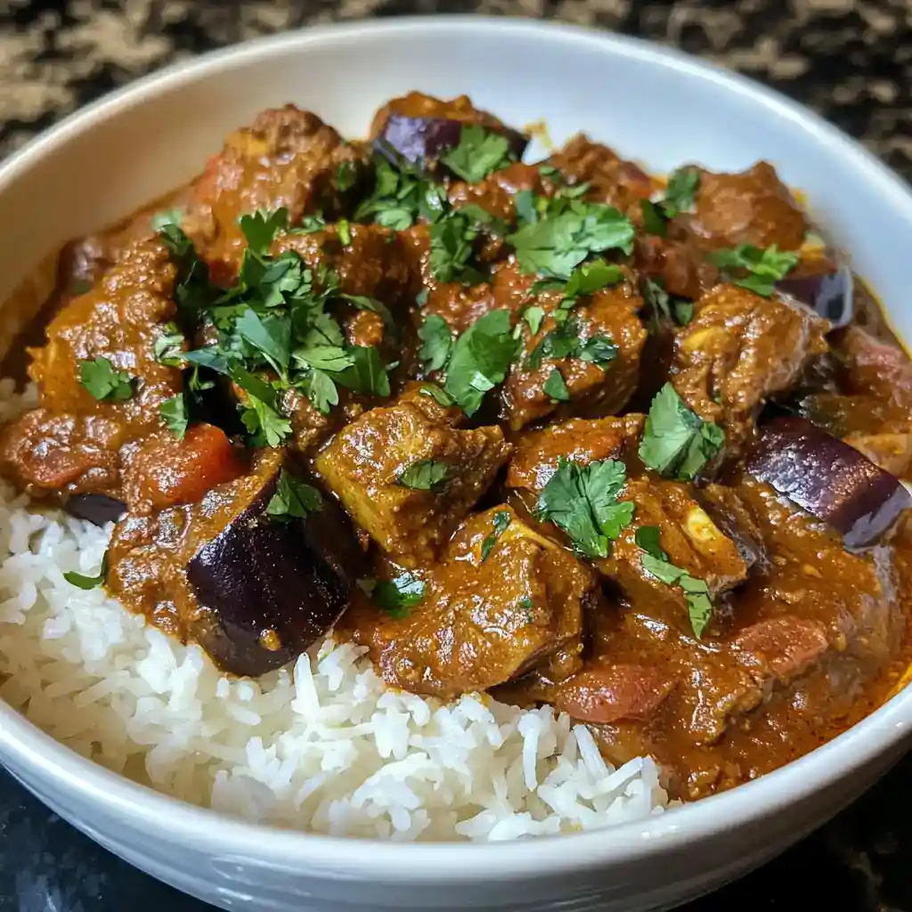 Delicious beef and eggplant curry served over fluffy white rice, garnished with fresh cilantro, perfect for a hearty and flavorful meal.