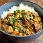 Hearty beef stew with carrots and herbs served over rice in a black bowl, perfect for comfort food lovers.