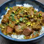 Delicious beef curry served over white rice, garnished with chopped pistachios and fresh herbs, perfect for a hearty meal.