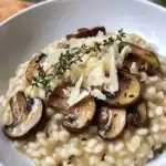Delicious creamy mushroom risotto topped with grated Parmesan cheese and fresh thyme, served in a white bowl. Perfect comfort food for mushroom lovers.